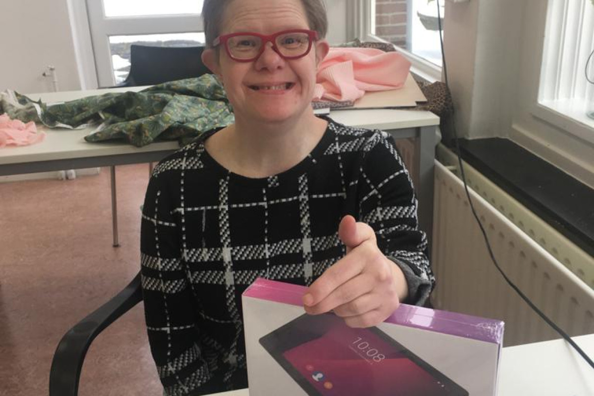 Een blije vrouwelijke deelnemer van dagbesteding de Molenkamp houdt trots een tablet in verpakking omhoog.